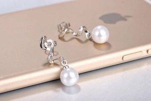 Macro view of silver spiral pearl earrings with diamond accents on a sleek surface