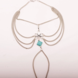 Detail of silver thigh chain featuring layered metal strands and turquoise square gemstones