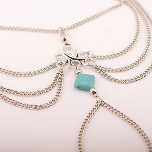 Detail of silver bohemian foot chain with hollow patterns and square blue turquoise charm