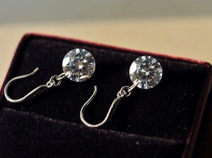 Macro shot of 8mm round brilliant-cut silver drop earrings on a purple velvet box