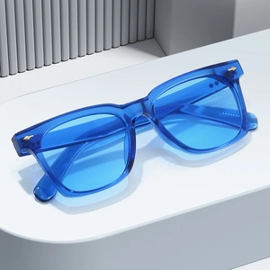 Modern blue transparent square sunglasses with gold arrow rivets on a minimalist pedestal