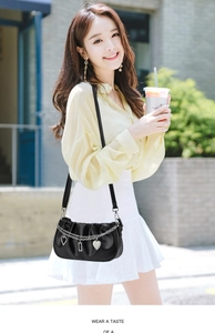 Detail of black pleated crossbody bag featuring silver chains and rhinestone heart charms