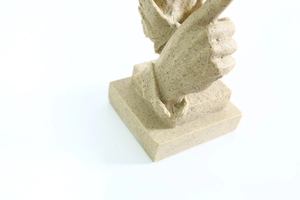 Gros plan d'une sculpture en résine beige montrant une main ailée faisant le geste chut