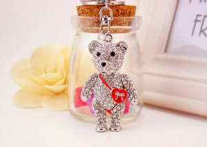 Close-up of a silver rhinestone-encrusted bear keychain with a red heart bag and bow