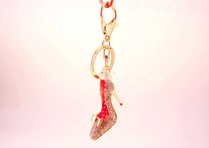 Gros plan d'un porte-clés escarpin doré avec strass, émail rose et nœud décoratif