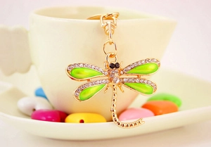 Detail of green enamel dragonfly keychain with white rhinestones on a ceramic cup
