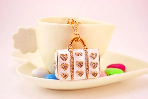 Detail view of a white enamel handbag keychain with gold trim and heart-shaped rhinestones
