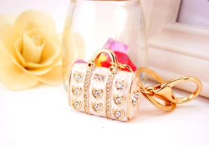 Detailed view of handbag keychain with white enamel, gold frames and heart-shaped crystals