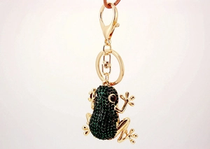 Close-up of a golden frog keychain with green rhinestones and red crystal eyes on white background