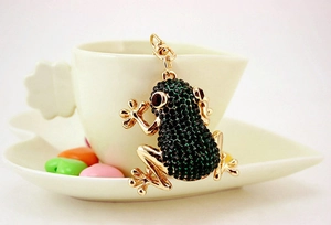Detail of a gold metal frog keychain with green rhinestones on a white heart saucer