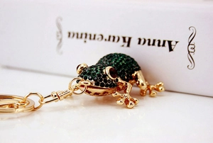Close-up of green rhinestone frog keychain on a white book with gold metal finish