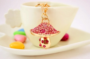 Dettaglio del portachiavi a fungo dorato con strass rosa appeso al bordo di una tazza