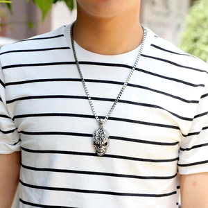 Silver skull pendant necklace on long box chain worn by a male model outdoors