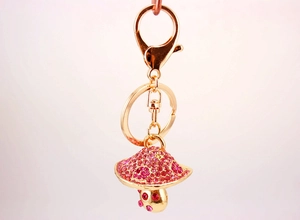 Close-up of golden keychain with a shiny pink rhinestone mushroom charm and lobster clasp
