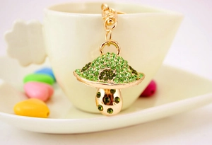 Dettaglio portachiavi a fungo con strass verdi appeso a una tazza di tè bianca