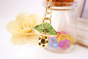Detail of green rhinestone mushroom keychain with gold metal clasp and floral background