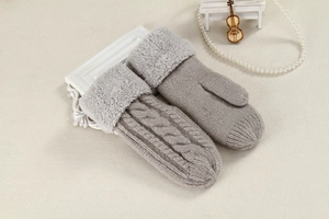 Detail of light gray cable knit mittens featuring elegant faux fur cuffs on beige fabric