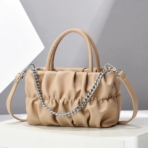 Elegant beige pleated crossbody bag with chain and leather strap on a minimalist plinth