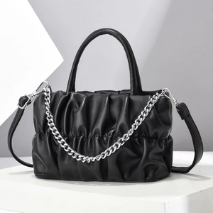 Pleated black crossbody bag with silver chain strap on a modern geometric display
