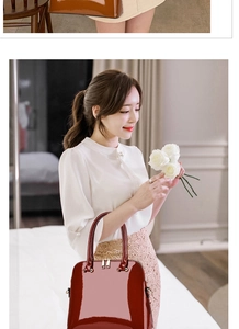 Detail of burgundy glossy shell bag with gold hardware held by a model in a soft setting