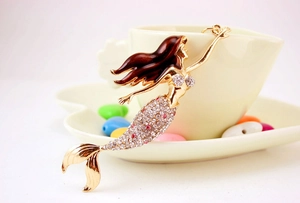 Close-up of golden mermaid keychain with pink rhinestones on white coffee cup background