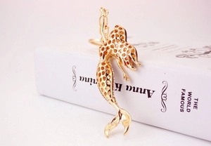 Close-up of golden rhinestone mermaid keychain with intricate cutout details on a book