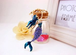 Detail of a golden mermaid keychain with blue crystals and enamel beside a photo frame