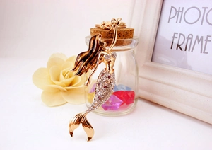 Detail of golden mermaid keychain with enamel hair and rhinestone tail on a white table