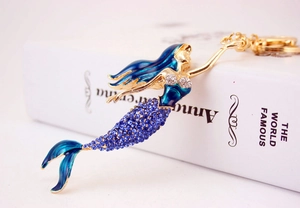 Detailed close-up of crystal-encrusted mermaid keychain with blue enamel work on a book