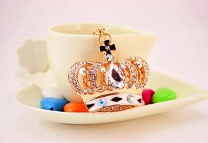 Close-up of golden crown keychain with crystals and enamel details on a tea cup