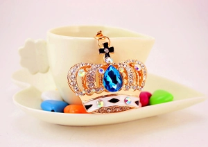 Detail of a golden crown keychain with clear rhinestones and a blue teardrop gemstone