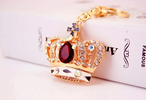 Close-up of golden crown keychain with sparkling crystals and red gemstone on book