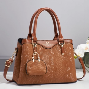 Brown faux-snakeskin handbag with top handle and gold bow logo on a minimalist background