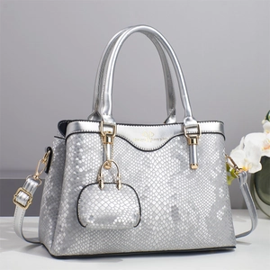 Detail of silver snake-textured handbag featuring a gold logo and a mini charm accessory