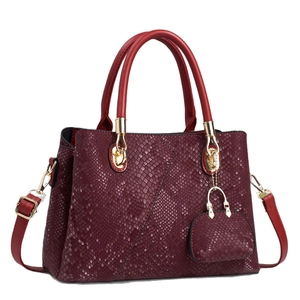 Burgundy faux snakeskin handbag with gold hardware and mini charm on white background