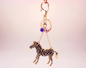 Detail of crystal zebra keychain with gold metal clasp and colorful beads on pink backdrop