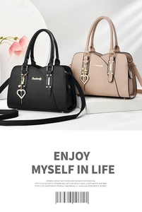 Detail of heart pearl charm and metal brand logo on textured leather crossbody bag