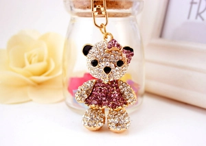 Close-up of golden keychain with sparkling rhinestone bear wearing a pink purple dress