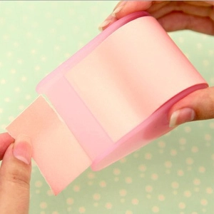 Pink sticky note tape dispenser used by hands over a soft green polka dot background