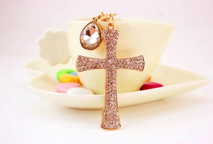 Close-up of sparkling gold cross keychain with teardrop rhinestone on a heart plate