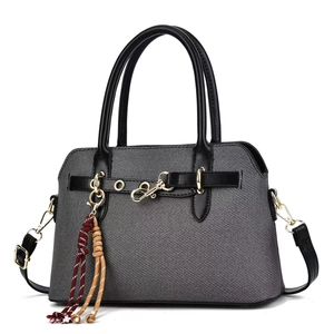 Détail du sac à main gris avec breloque papillon dorée et gland tissé décoratif