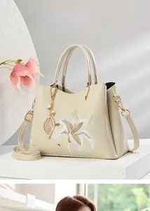 Details einer eleganten beige Handtasche mit feiner Lilienstickerei und goldenem Anhänger