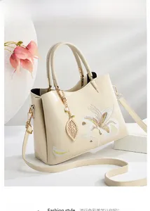 Detail der eleganten beige Handtasche mit weißer Blumenstickerei und goldenem Blattanhänger