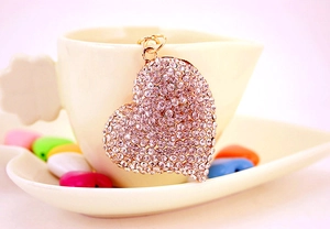 Sparkling white rhinestone heart keychain with gold ring hanging on a cream teacup