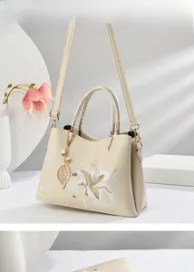 Detail der Lilienstickerei und des Perlenanhängers an einer beigen Handtasche