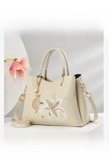 Nahaufnahme der Lilienstickerei und des Goldblatt-Anhängers auf beiger Ledertasche