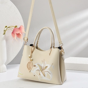 Elegante cremeweiße Handtasche mit Blumenstickerei und Blattanhänger im Fotostudio