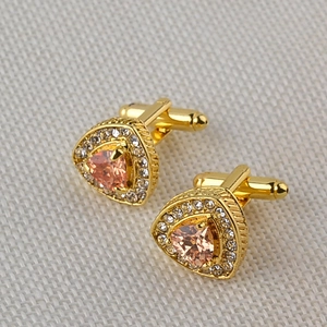 Detailed macro of golden cufflinks with triangular pink crystal and diamond accents