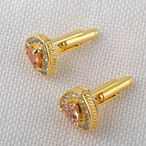 Macro detail of pear-shaped pink crystal cufflinks with gold-plated setting and white stones