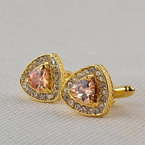 Macro view of gold-plated cufflinks featuring a triangular orange crystal and white diamonds